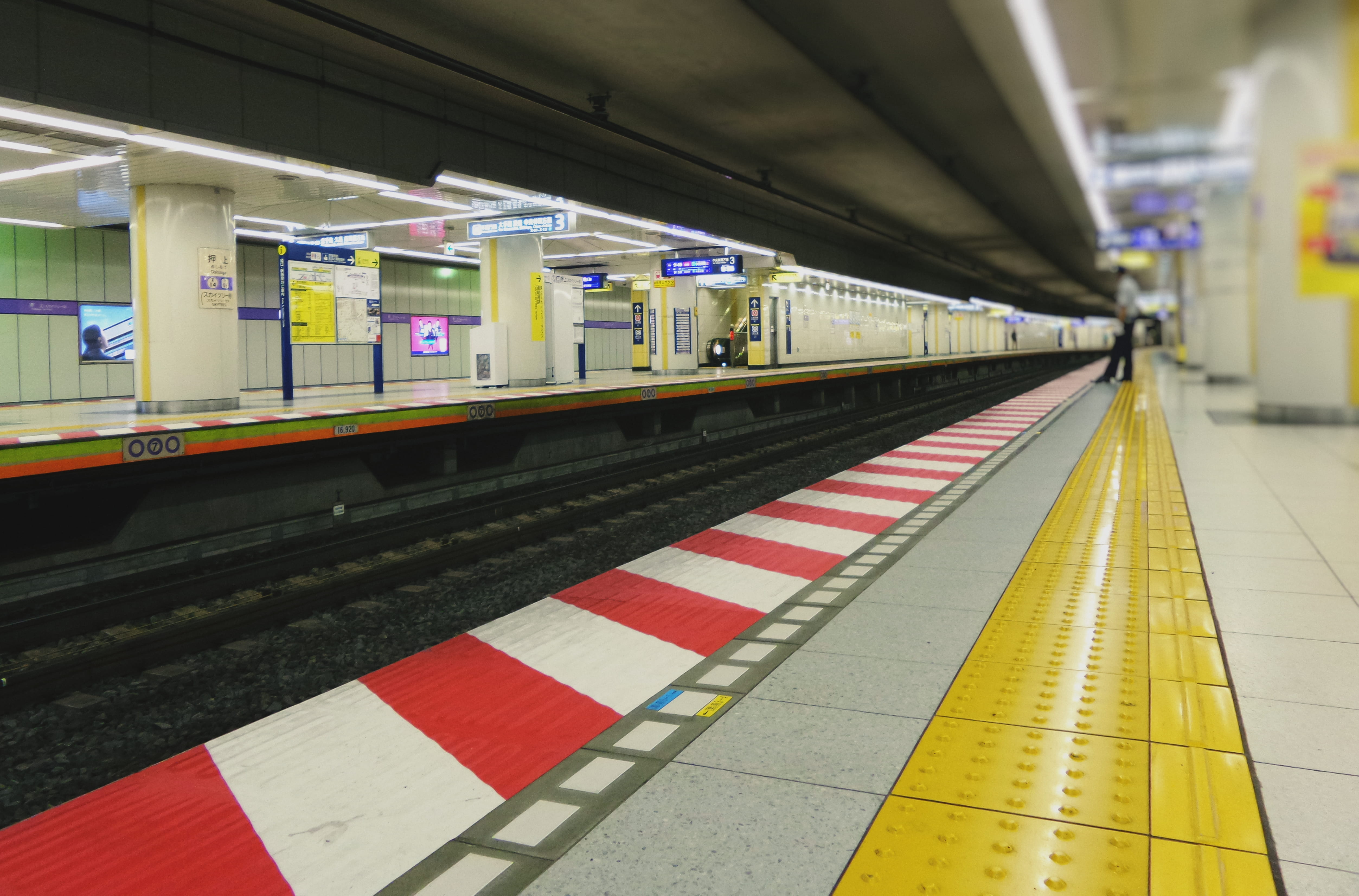 A clean, modern Tokyo train station platform with a train arriving, displaying organized queues of people waiting patiently behind yellow lines.