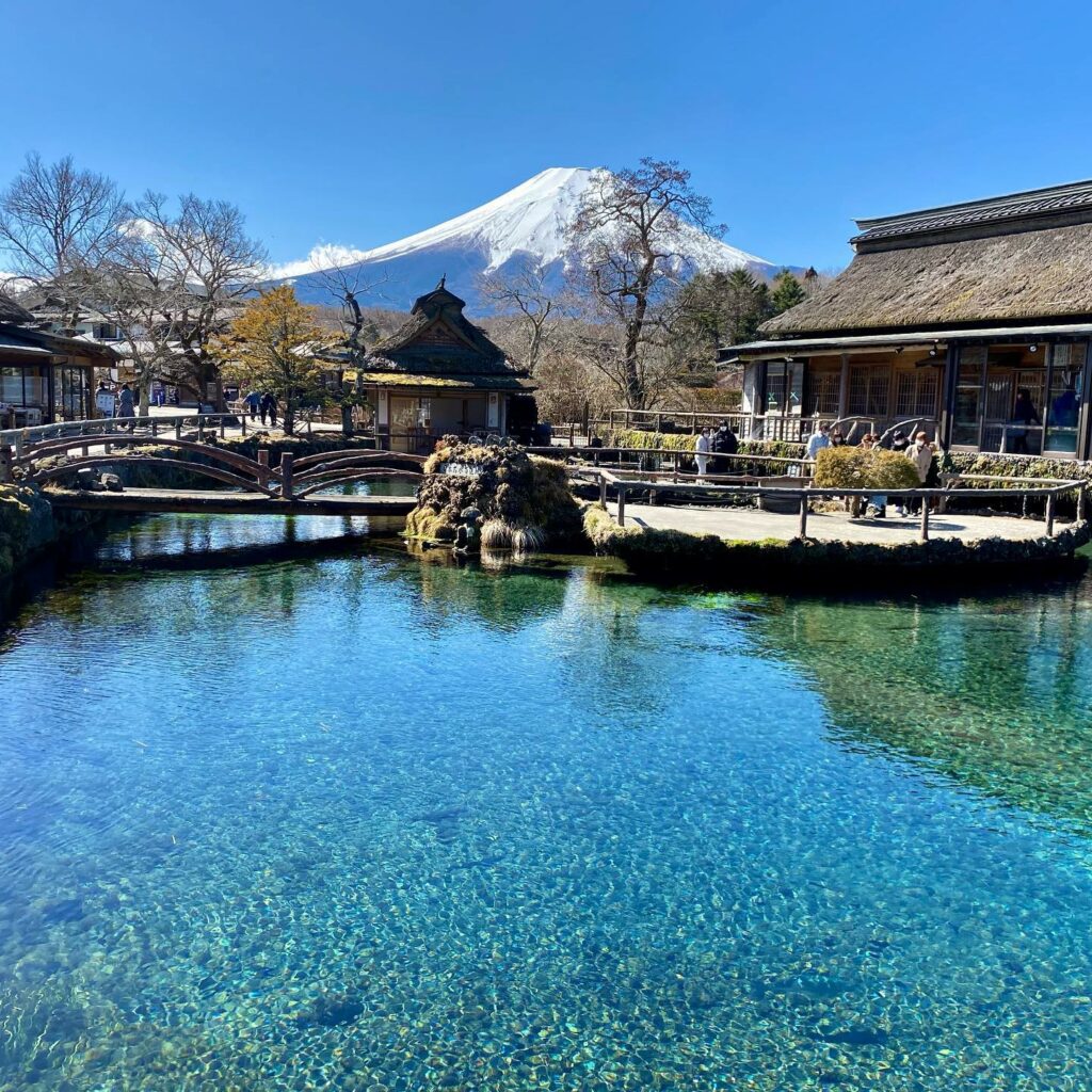 One of the crystal-clear ponds of Oshino Hakkai village, with traditional Japanese houses and a view of Mount Fuji in the distance.