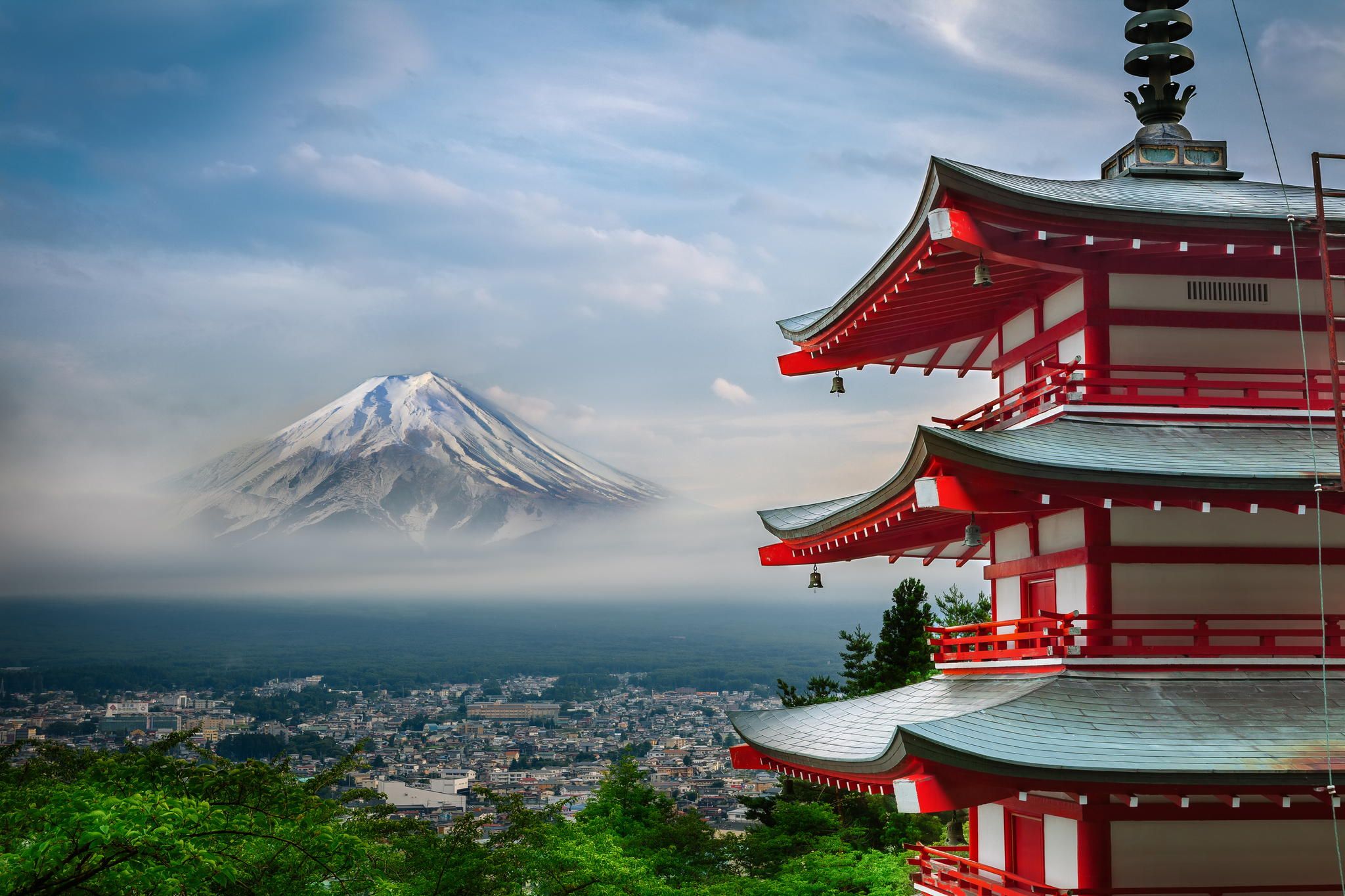 The iconic five-story Chureito Pagoda in the foreground, with the snow-capped Mount Fuji in the background, surrounded by blooming cherry trees.