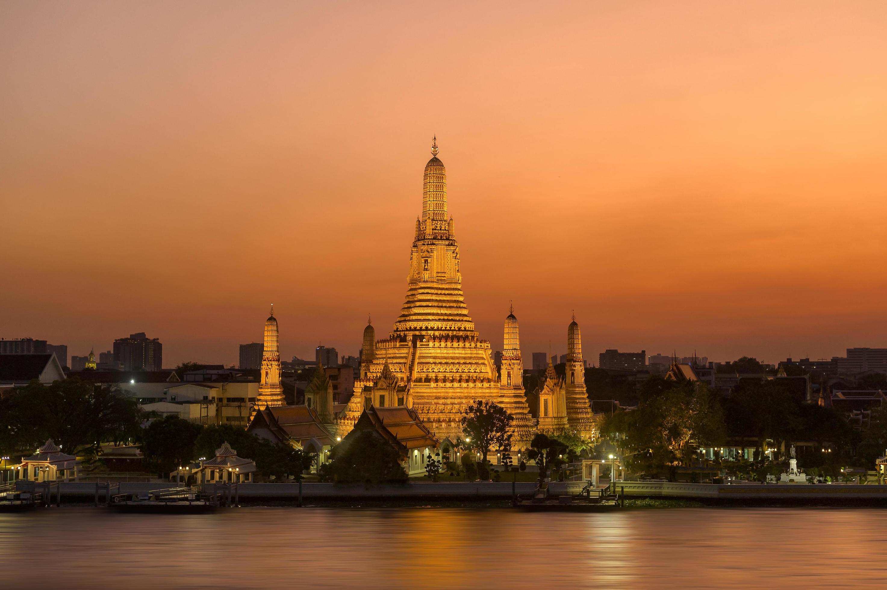 Wat Arun, the Temple of Dawn, illuminated against a sunset sky.