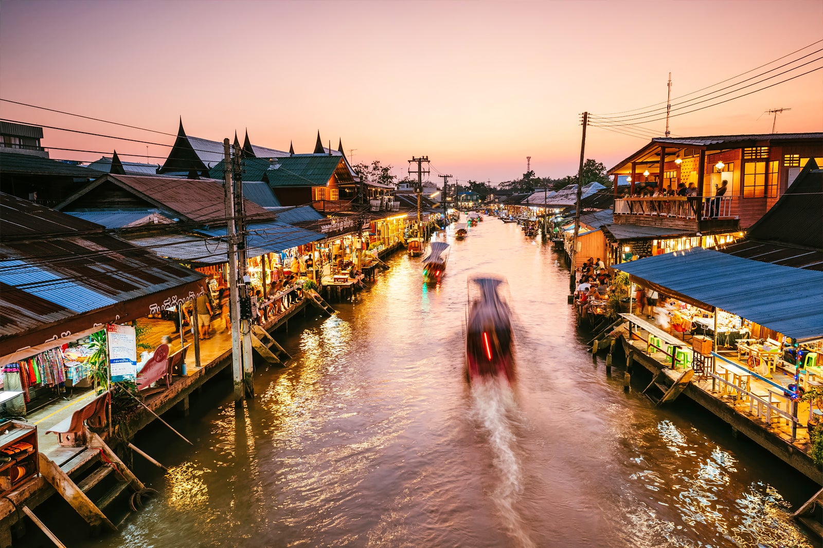Amphawa Floating Market bustling at dusk with illuminated boats.