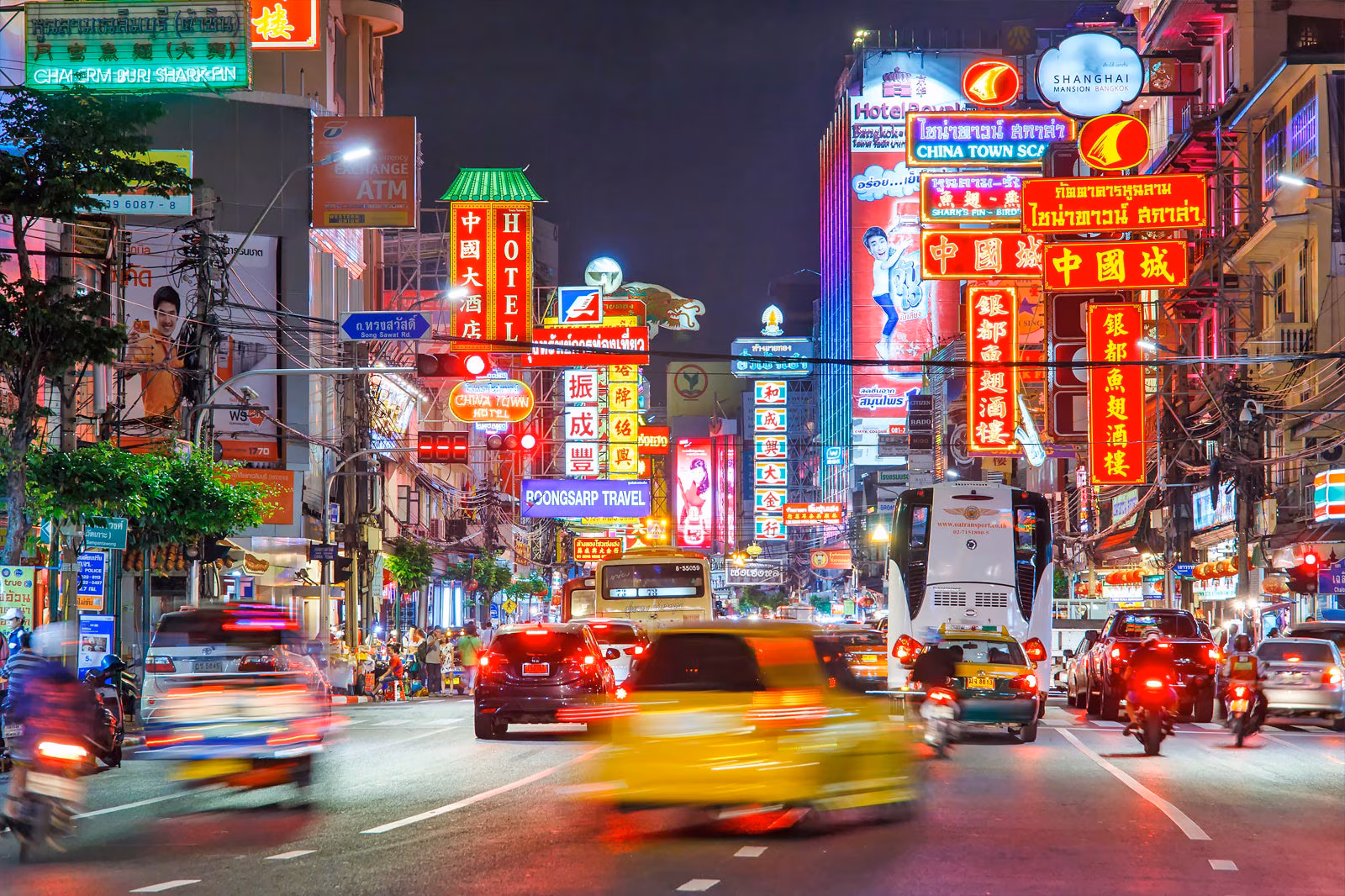 A lively street scene in Bangkok's Chinatown at night with neon lights and street food stalls.