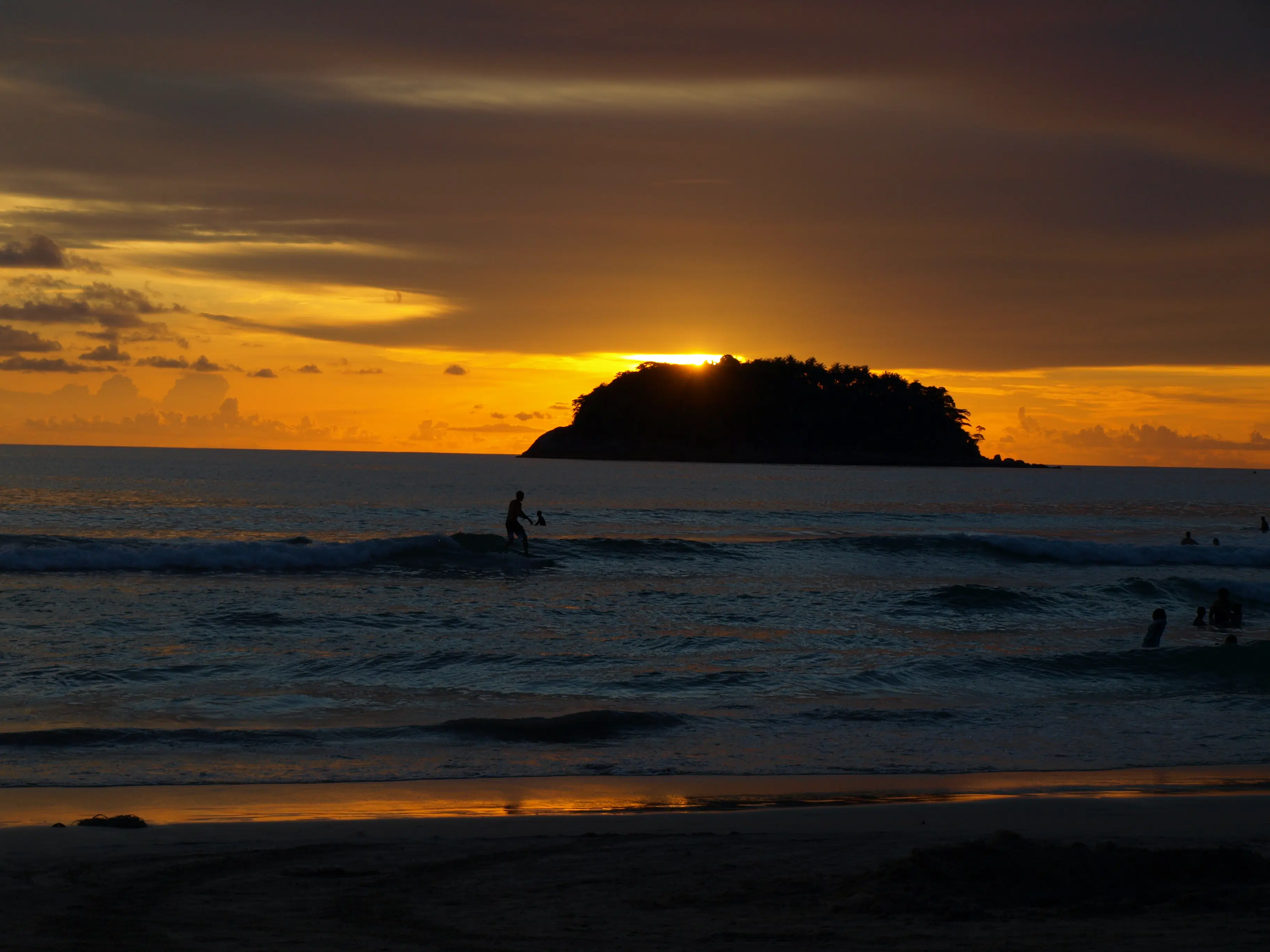 A beautiful sunset view over Kata Beach, with calm waves and palm trees.