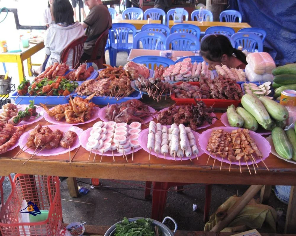 A street food vendor in Sapa grilling skewers of marinated meat and vegetables on a charcoal grill.