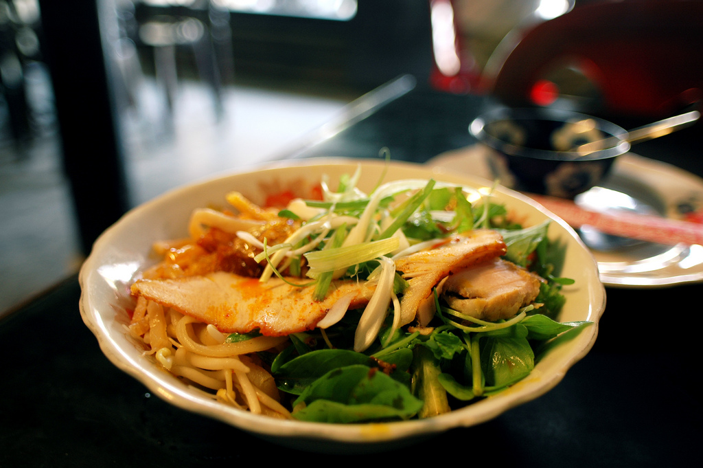 A bowl of Hoi An's signature dish, Cao Lau, with thick rice noodles, sliced pork, fresh greens, and crispy pork rinds on top.