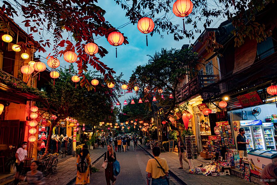 A bustling scene at Hoi An's Night Market, with a river in the background reflecting the light of hundreds of colorful, glowing silk lanterns.