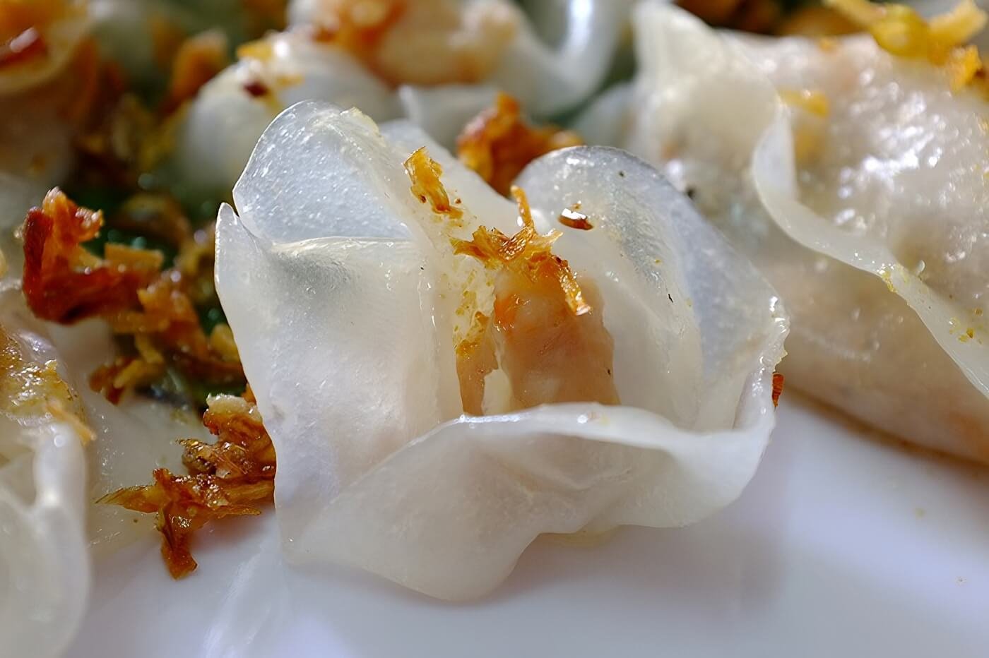 A plate of translucent White Rose dumplings, garnished with crispy fried shallots, ready to be dipped into sauce.