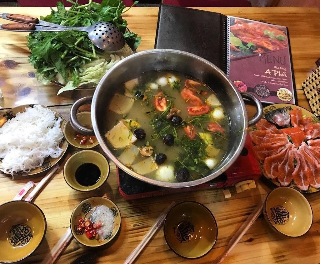 A bubbling pot of traditional Sapa hotpot with fresh vegetables, mushrooms, and meat being cooked on a burner in the center of a table.